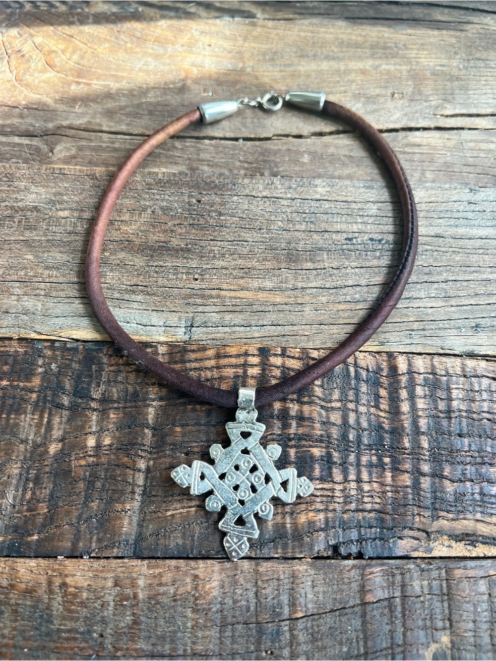 brown cord paired with a silver-toned pendant resembling an Ethiopian cross
